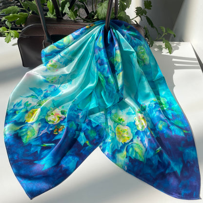 The Blue Rose scarf draped over a handbag, showing pale flowers and blue-green foliage