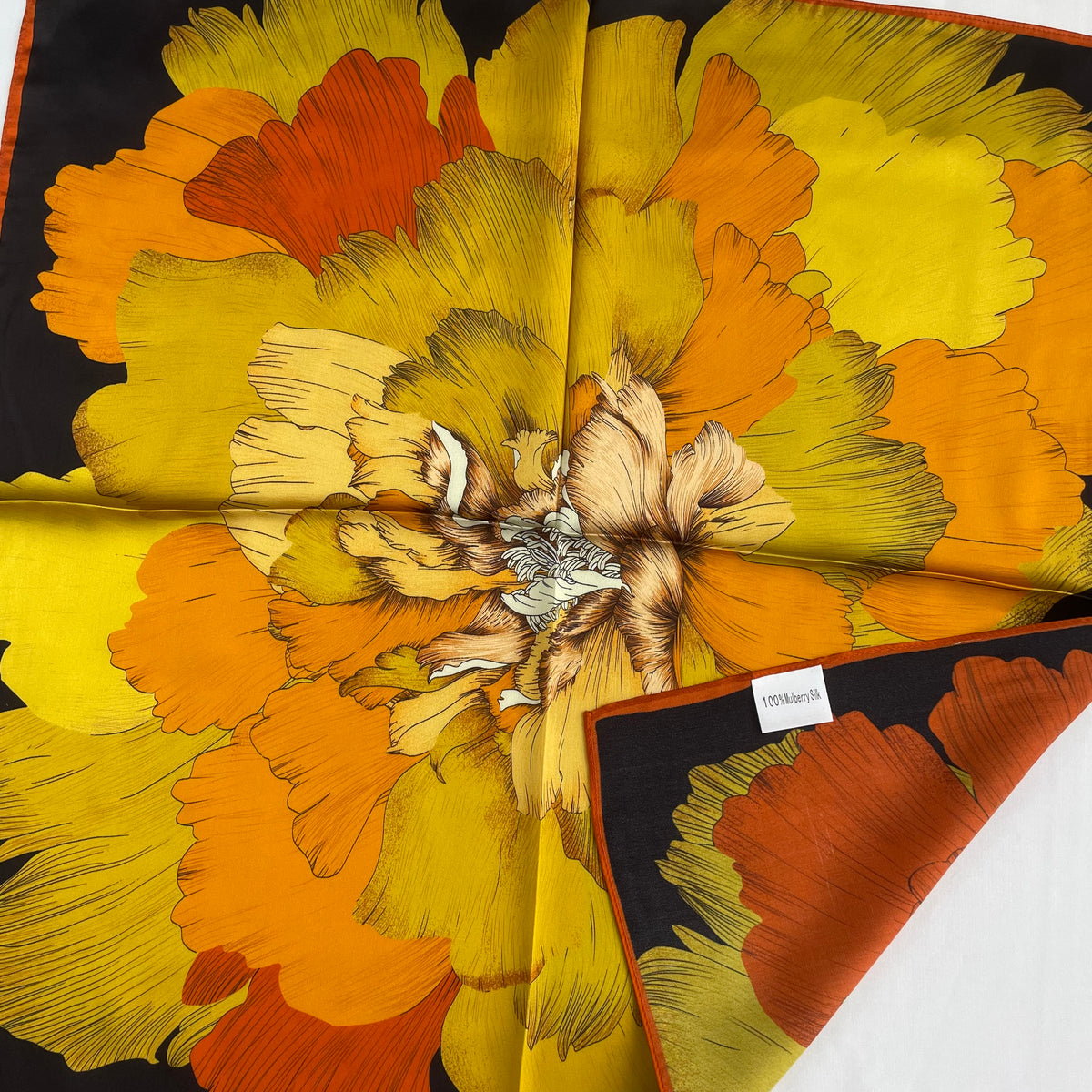 The Golden Flowers scarf with a corner folded back to show the reverse and mulberry silk label