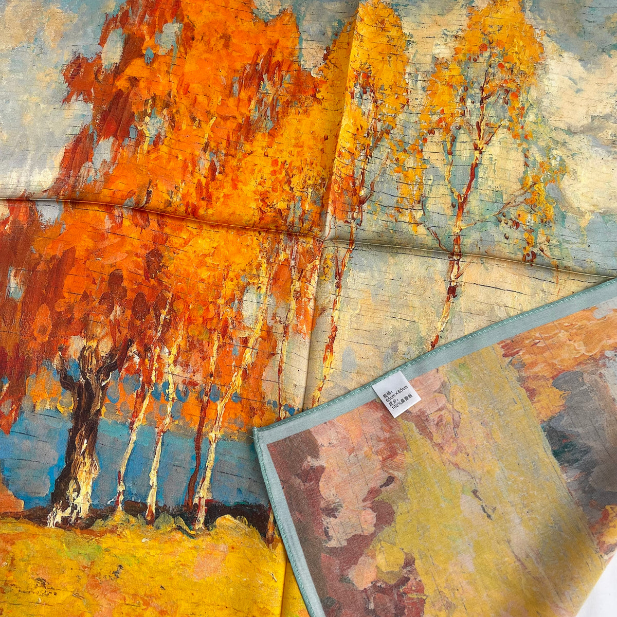 The Autumn Painting scarf with a corner folded back to show the reverse print, edge and fabric label
