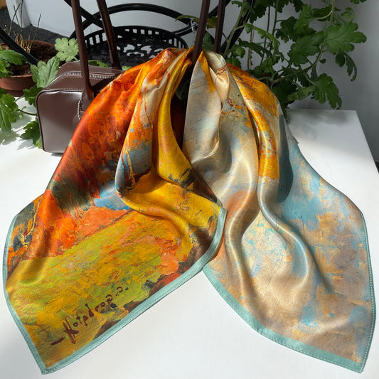 The Autumn Painting scarf draped over a brown handbag, showing orange and blue landscape colours