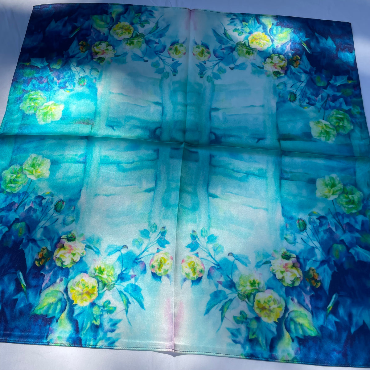 The Blue Rose scarf laid flat in sunlight, showing pale flowers around a blue and turquoise centre