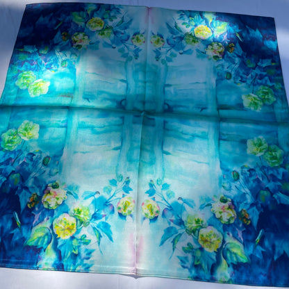 The Blue Rose scarf laid flat in sunlight, showing pale flowers around a blue and turquoise centre