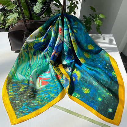 The Irises scarf draped over a handbag, showing blue flowers, green leaves and a yellow edge