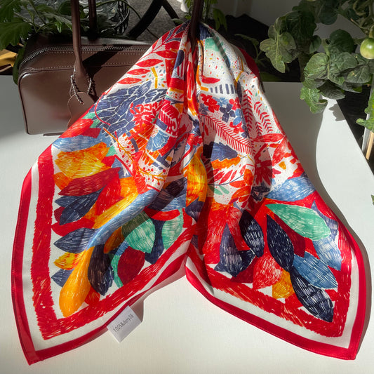 The Painting scarf draped over a handbag, showing a multicoloured floral and leaf print