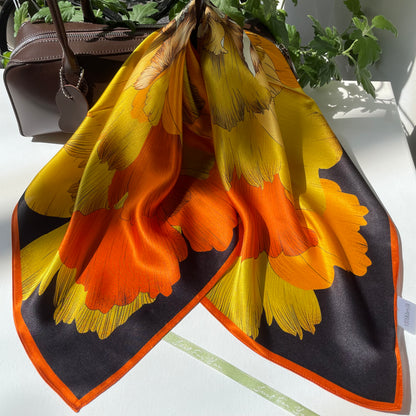 Wider handbag display of The Golden Flowers scarf, showing its orange edge and golden floral print