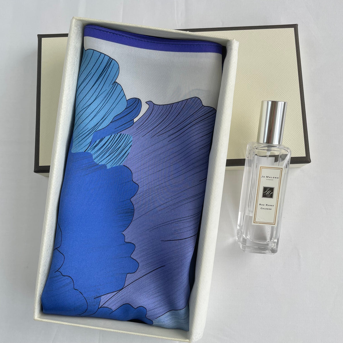 The Blue Flowers scarf folded in an open cream gift box beside a perfume bottle