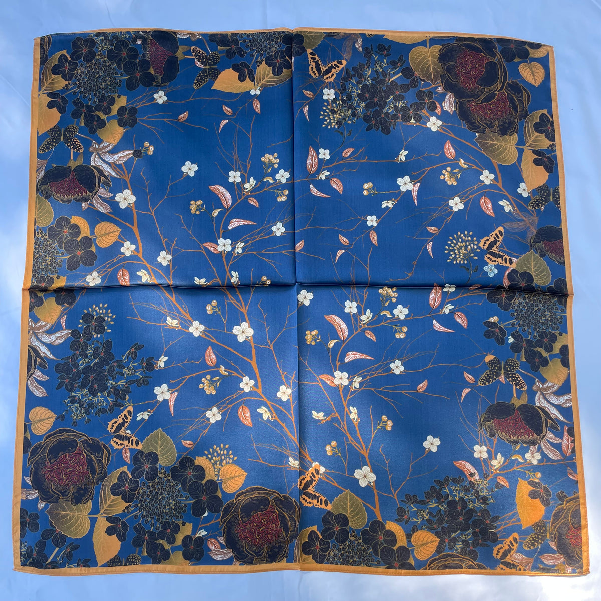 The Garden scarf laid flat, showing fine flowering branches on blue and a gold border