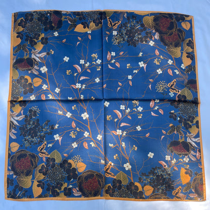 The Garden scarf laid flat, showing fine flowering branches on blue and a gold border