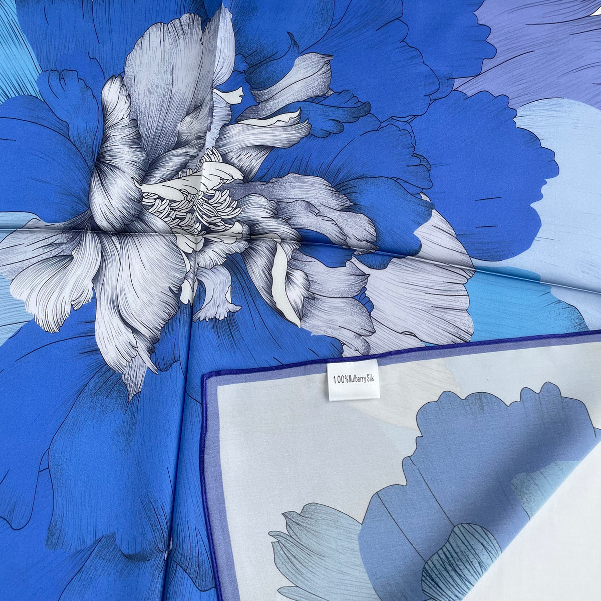 Close-up of The Blue Flowers scarf's blue petals, border and mulberry silk label