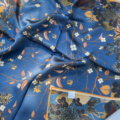 The Garden scarf loosely gathered, showing white blossoms on blue, a gold edge and fabric label