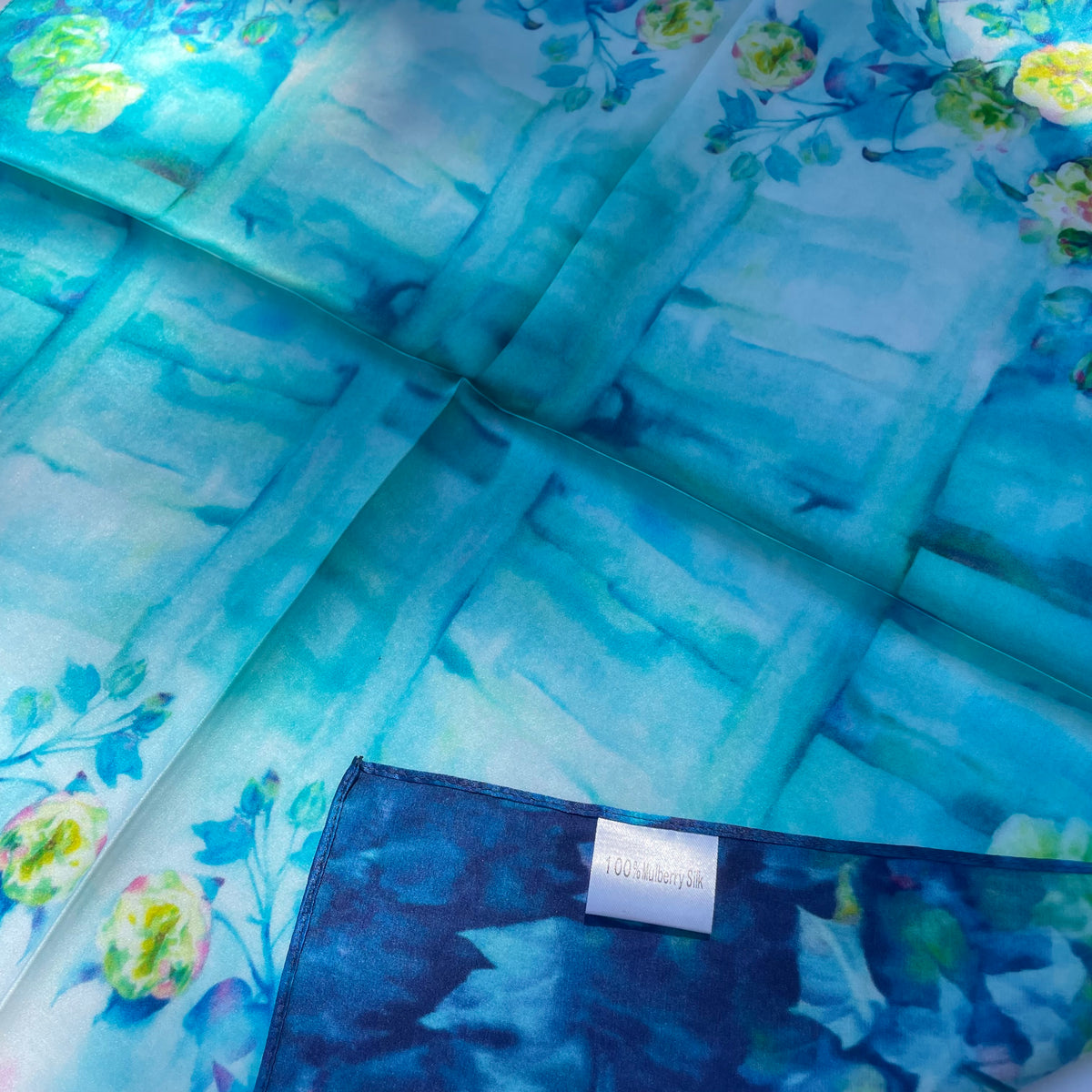 Close-up of The Blue Rose scarf's blue floral edge and mulberry silk label