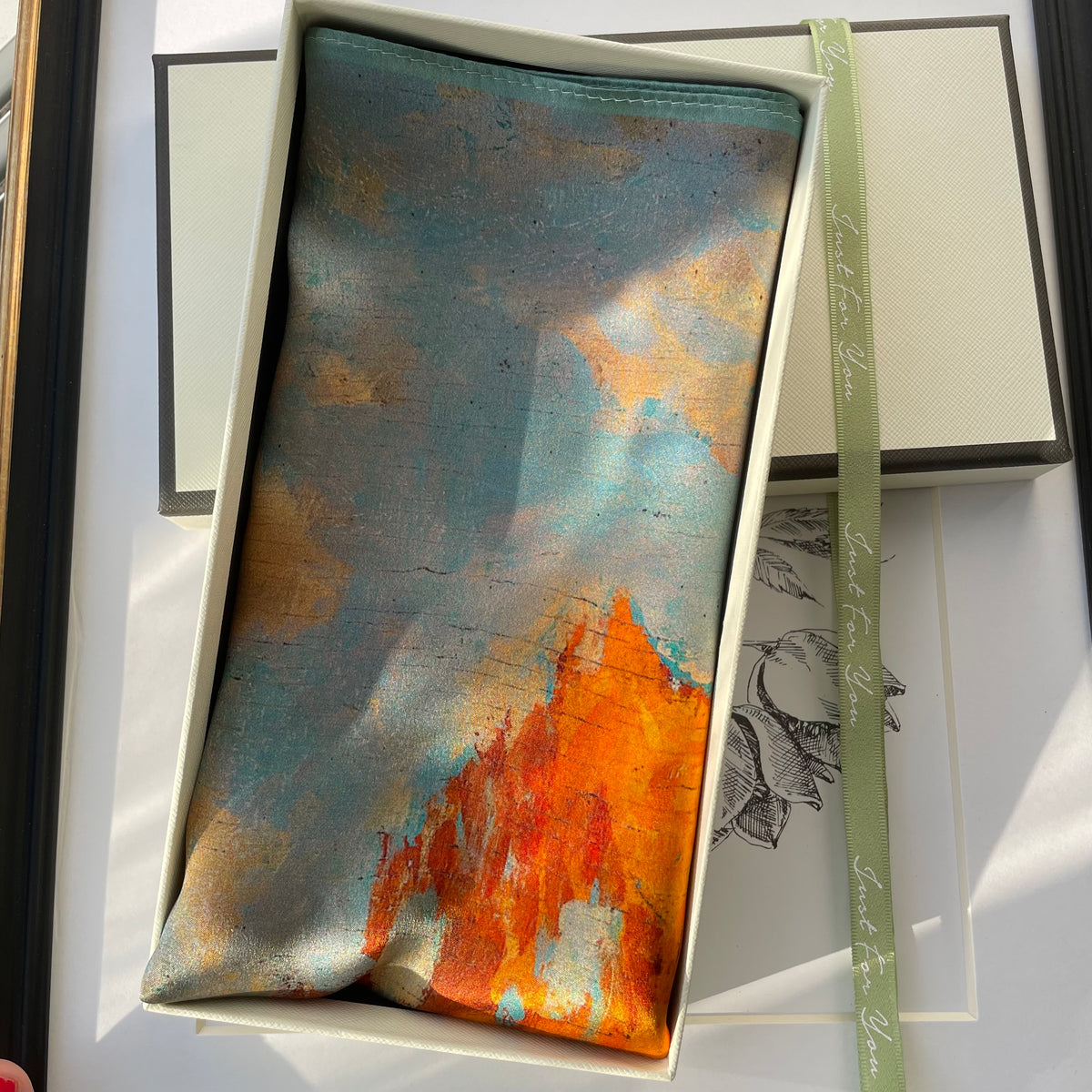 The Autumn Painting silk scarf folded in an open cream gift box, showing orange trees and blue tones
