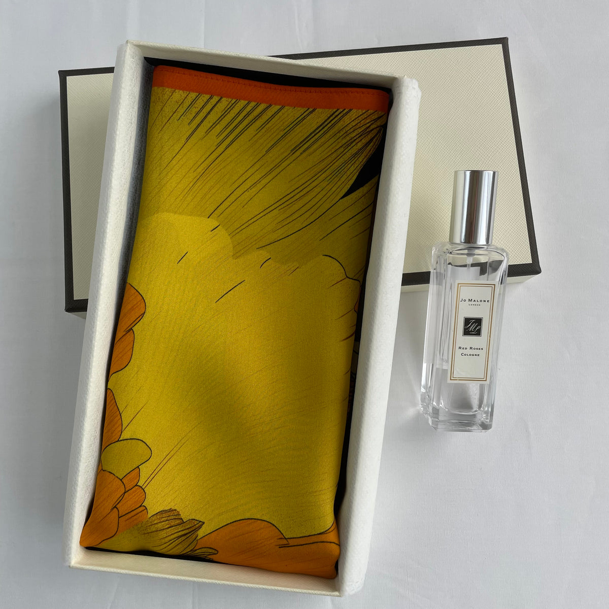 The Golden Flowers scarf folded in an open cream gift box beside a perfume bottle