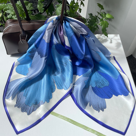 The Blue Flowers scarf draped over a handbag, showing oversized blue petals on white